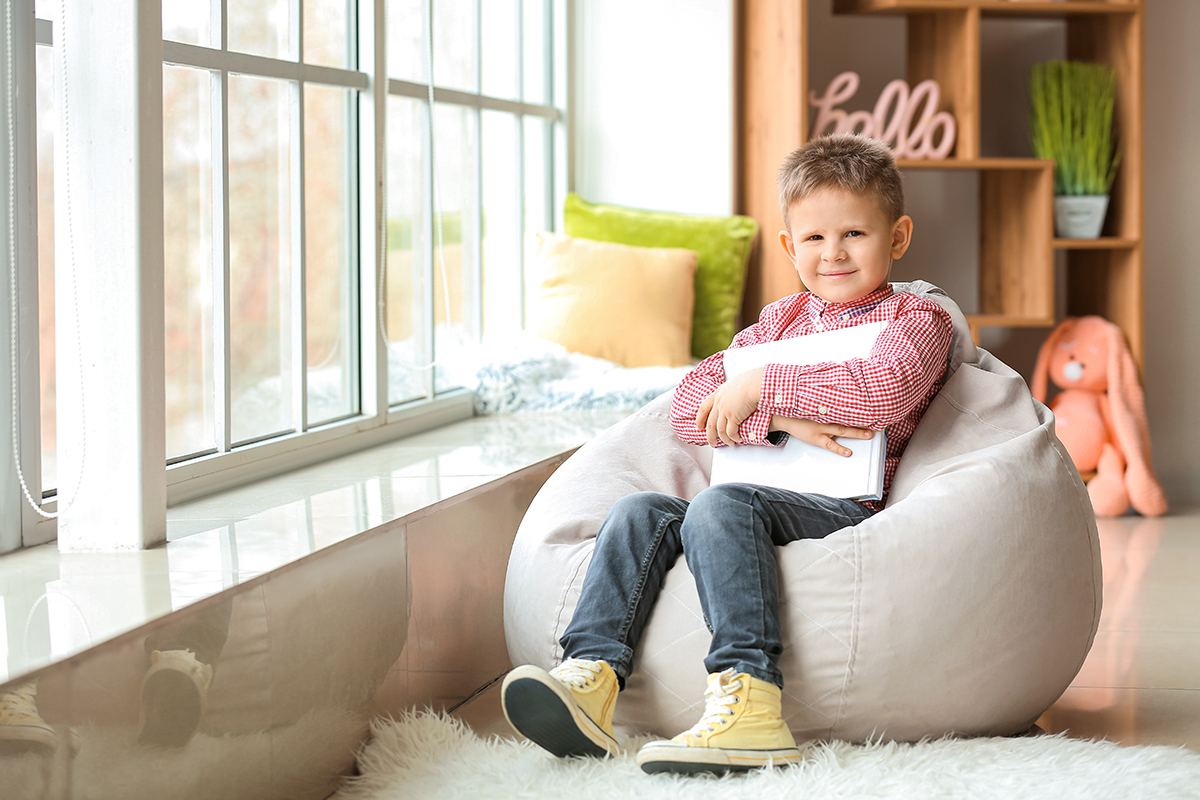 Photo d'un petit garçon assis sur un pouf avec un livre dans les bras